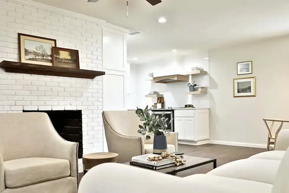Green Acres living room with a painted white brick fireplace and wood mantel