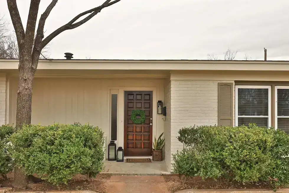 Green Acres after the renovation, the saved solid wood front door with a wreath between two shrubs