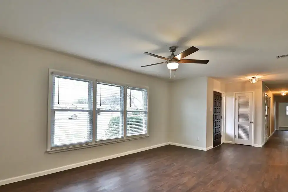 An empty Green Acres living room with wood floors and light from two windows