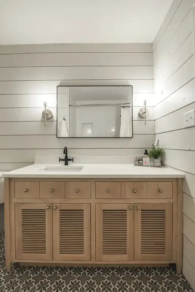 Lake house bathroom with a shiplap wall, a wood vanity and round mirror