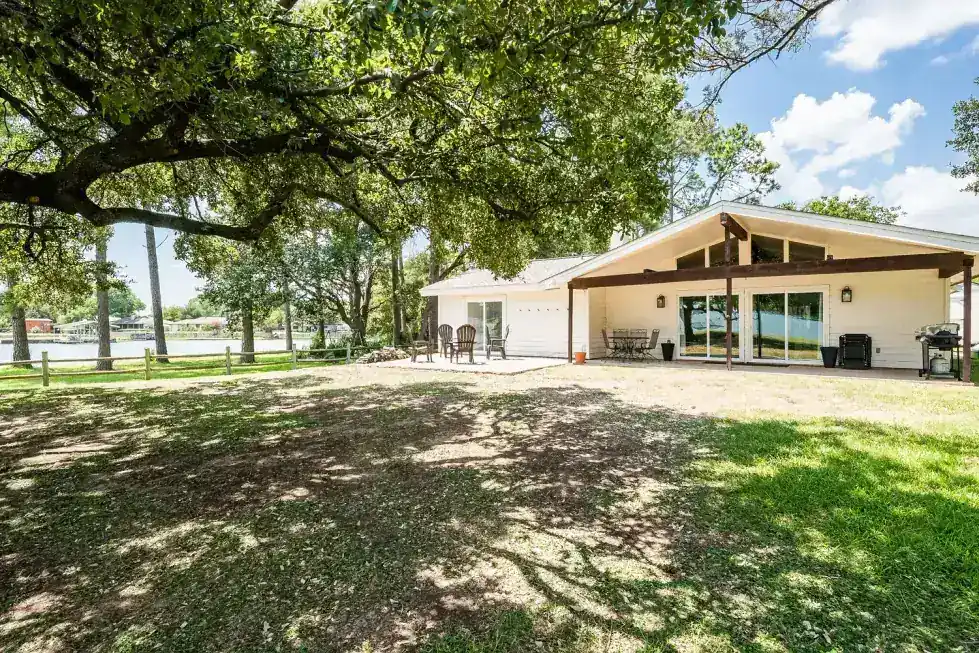 The lake house from the back lawn, a covered porch under big oaks with the lake behind